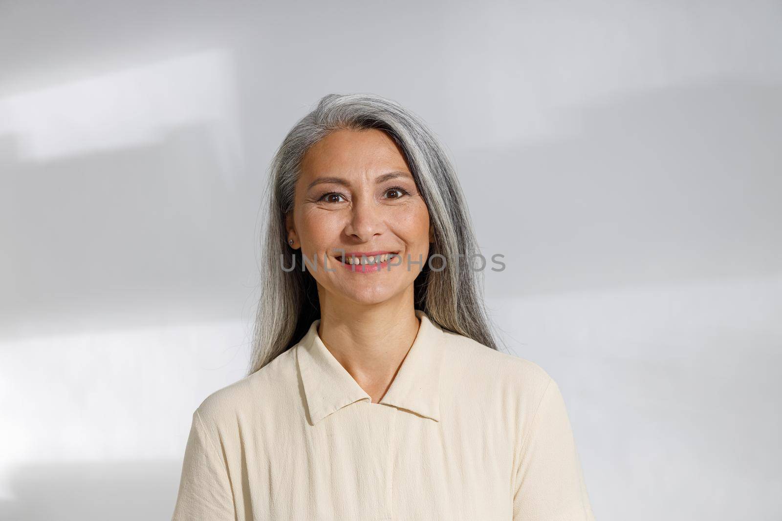 Portrait of pretty grey haired woman in beige blouse on light background by Yaroslav_astakhov