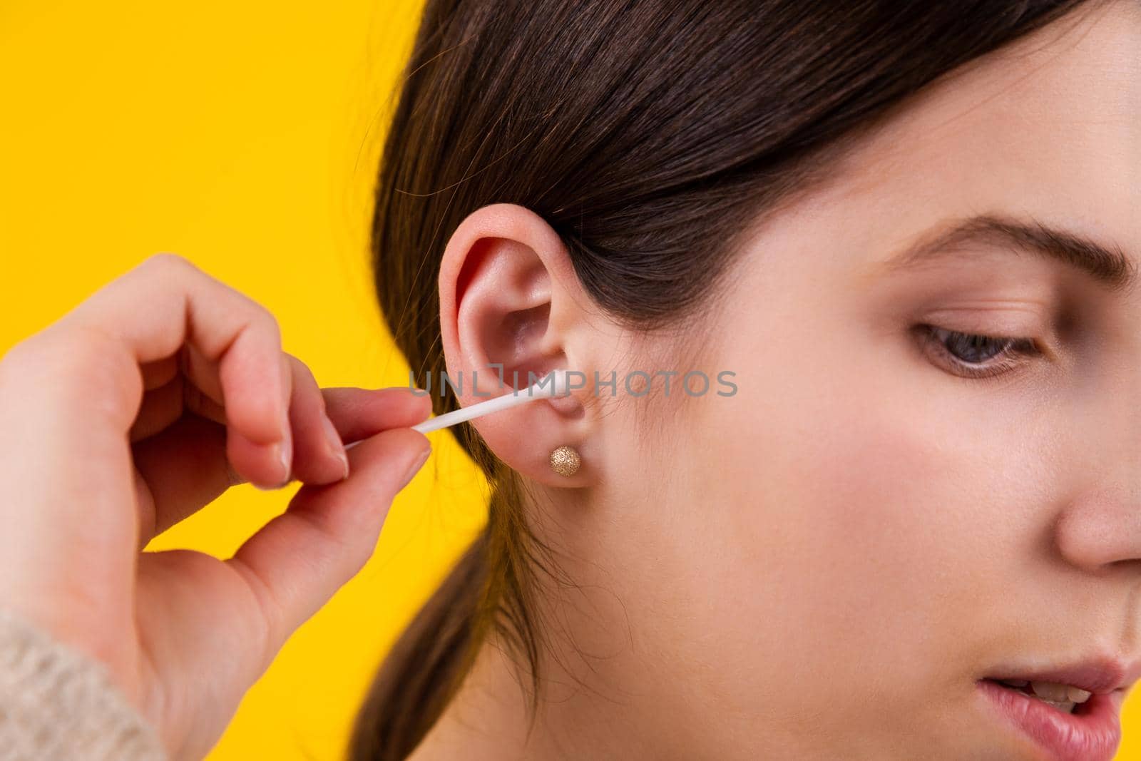 Young woman cleaning her ears with cotton sticks on yellow background