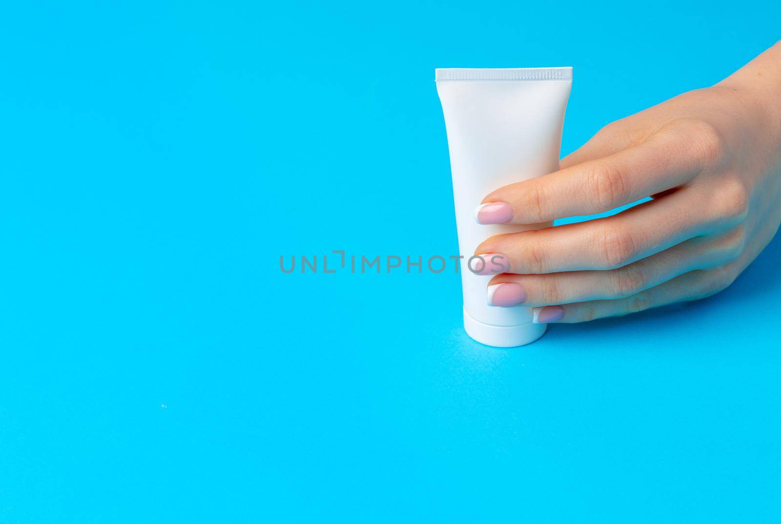 Female hand holding skincare product bottle on blue background