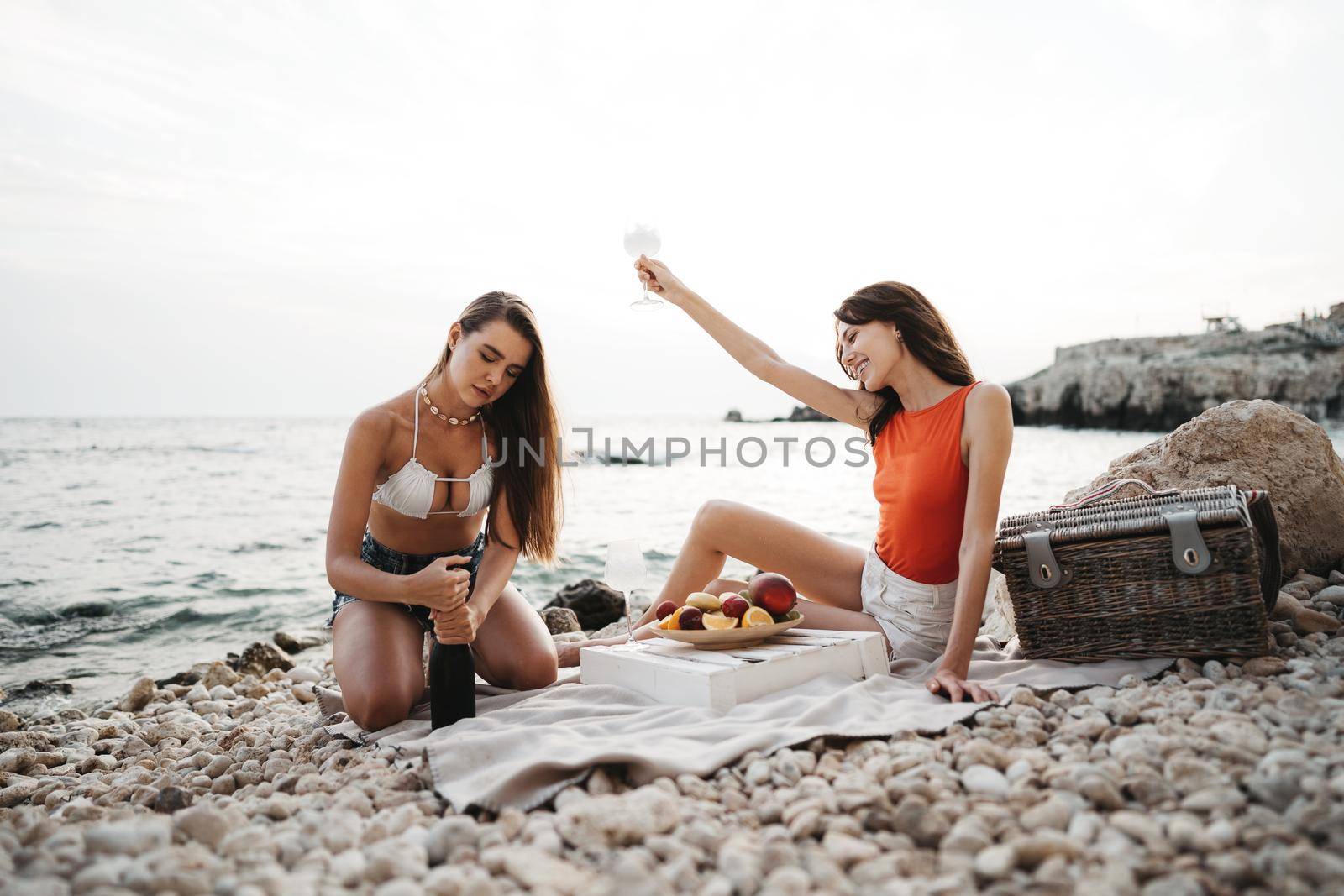 Two young female friends having a picnic on a beach drinking cocktails