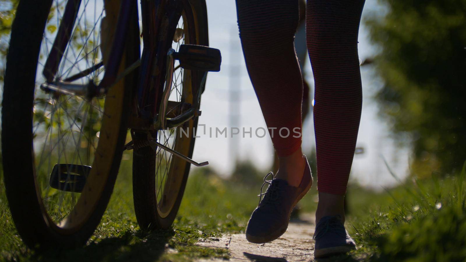 Legs of girls with bicycles on the path in the Park, against the green on a Sunny summer day, telephoto shot