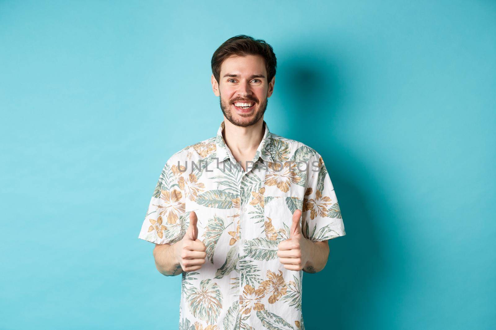 Summer holiday. Happy tourist showing thumbs up in approval and smiling, wearing hawaiian shirt, recommending travel agency, blue background by Benzoix