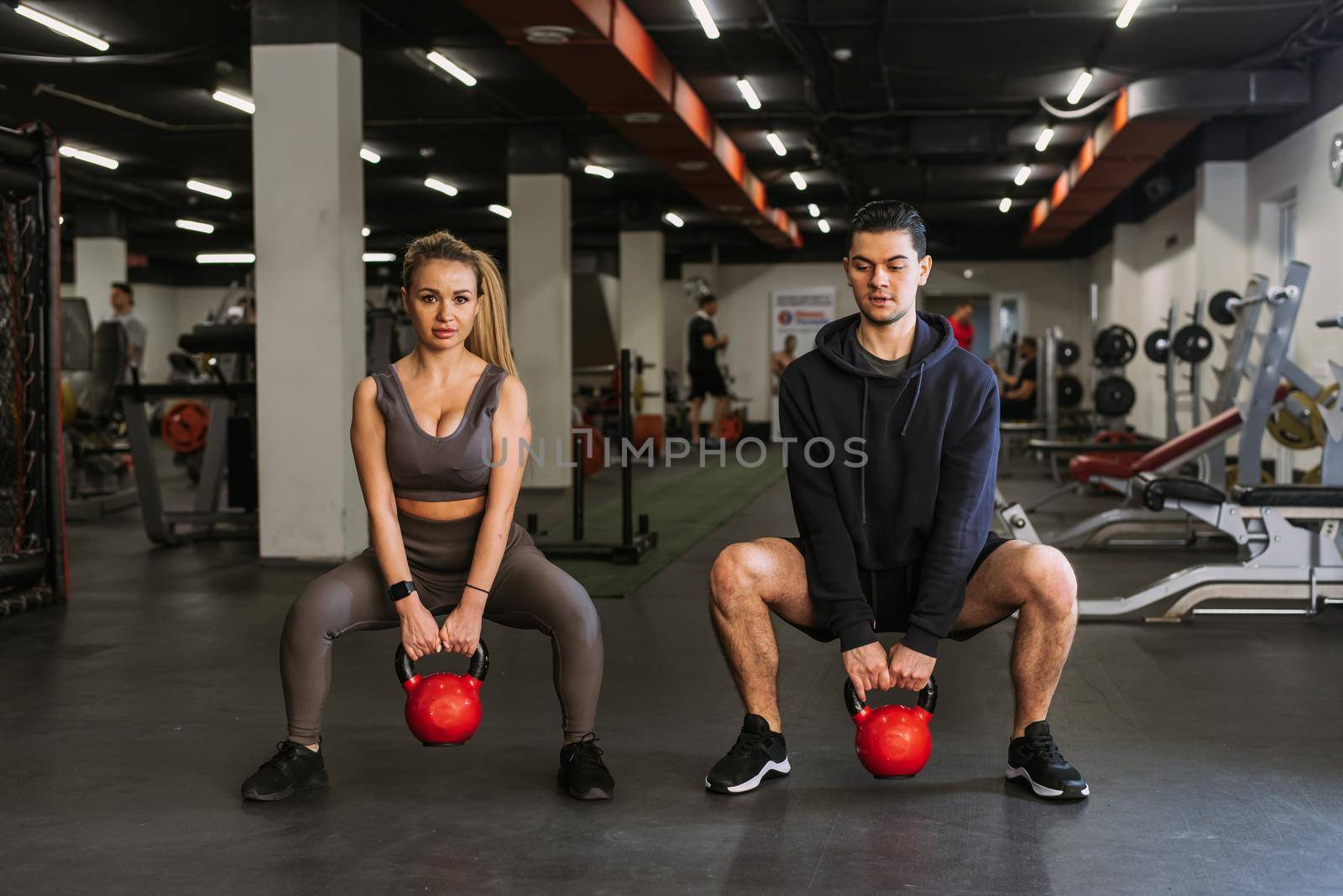 Fitness couple in sportswear squatting with weights and doing squats in the gym. A personal trainer in the gym corrects the squats of a young athlete.