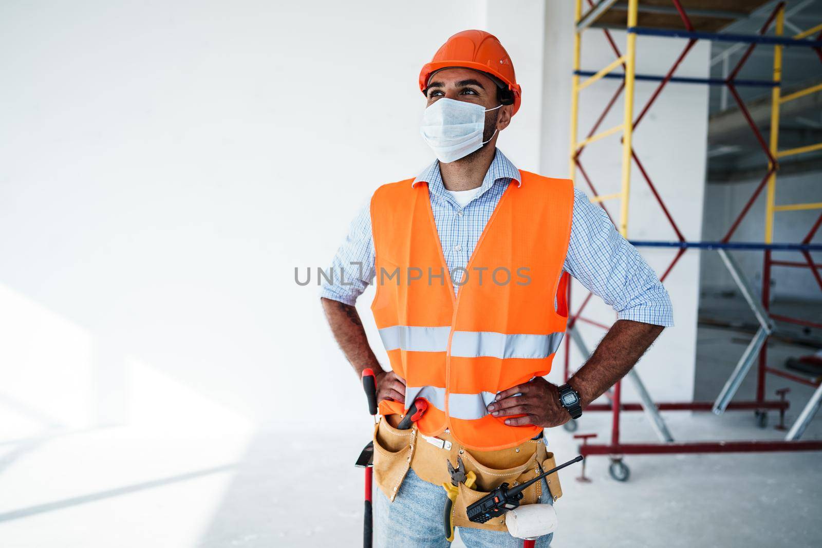 Portrait of mixed race man builder in workwear and hardhat wearing medical mask, close up photo