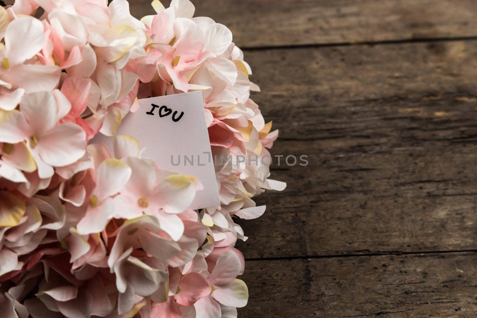 Pastel pink hydrangea flowers and a piece of paper on wood background. Copy space for text.