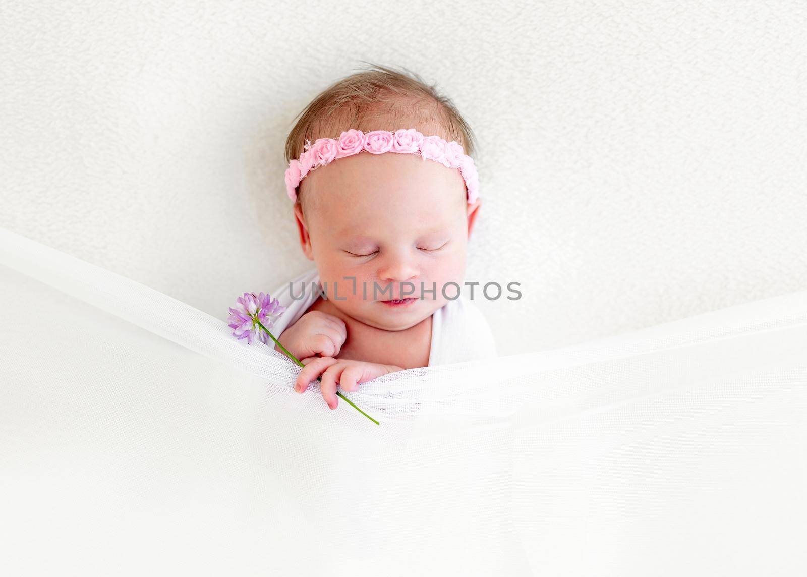 Sleeping newborn baby girl with flowers wrapped in white blanket
