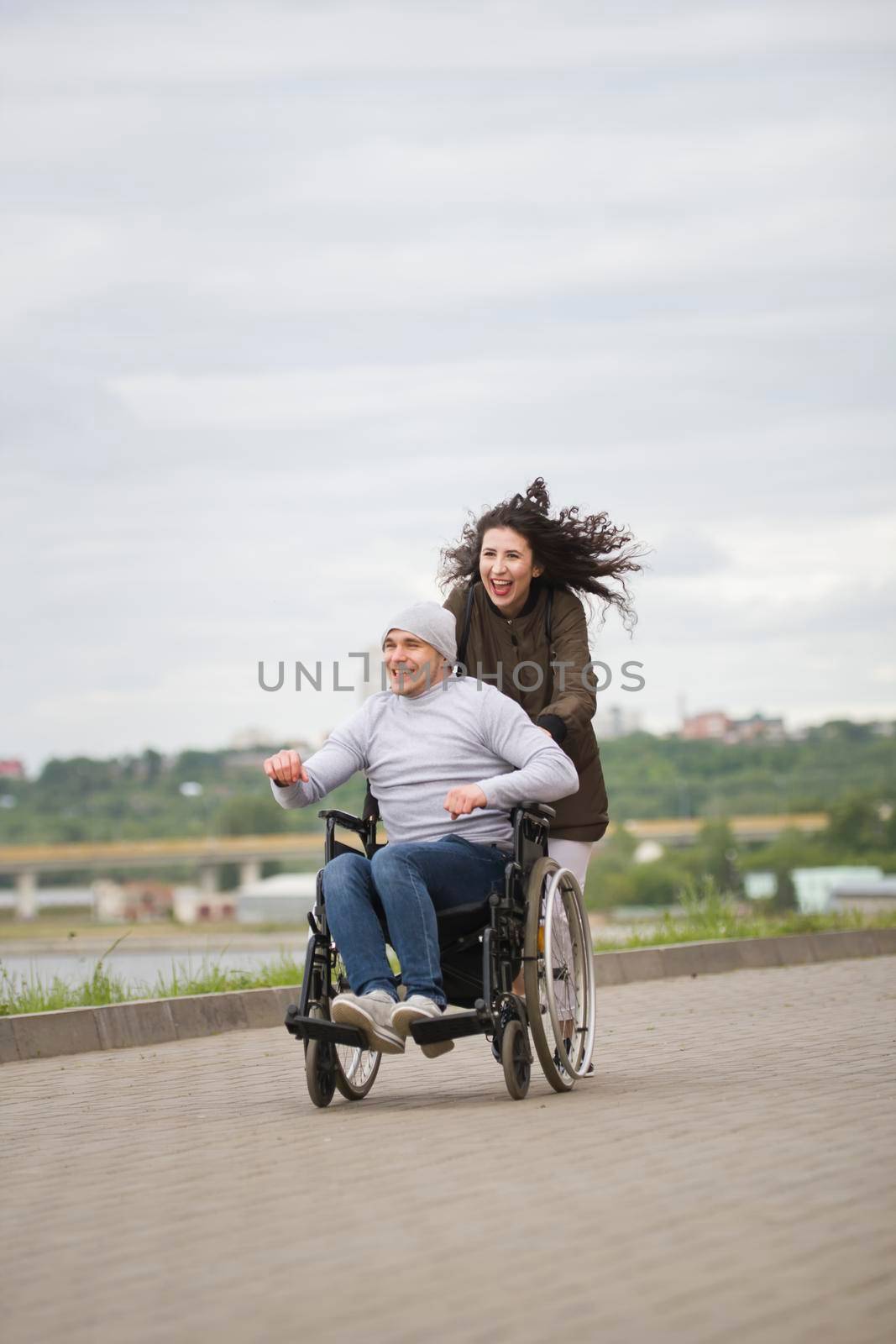 Beautiful woman with happy disabled man having fun outdoors in cloudy day, close up