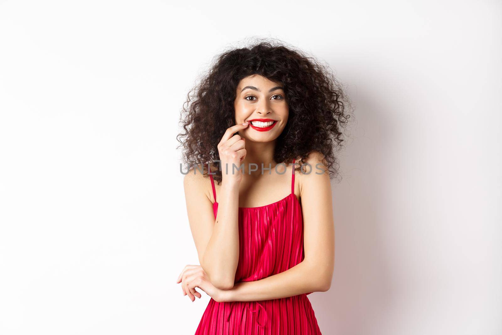 Excited beautiful woman in red dress, biting finger and smiling cute at camera, want something, standing on white background by Benzoix