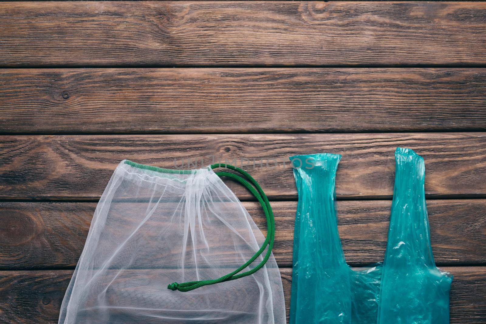 Reusable mesh eco bag vs plastic package on a wooden background. Zero waste concept.