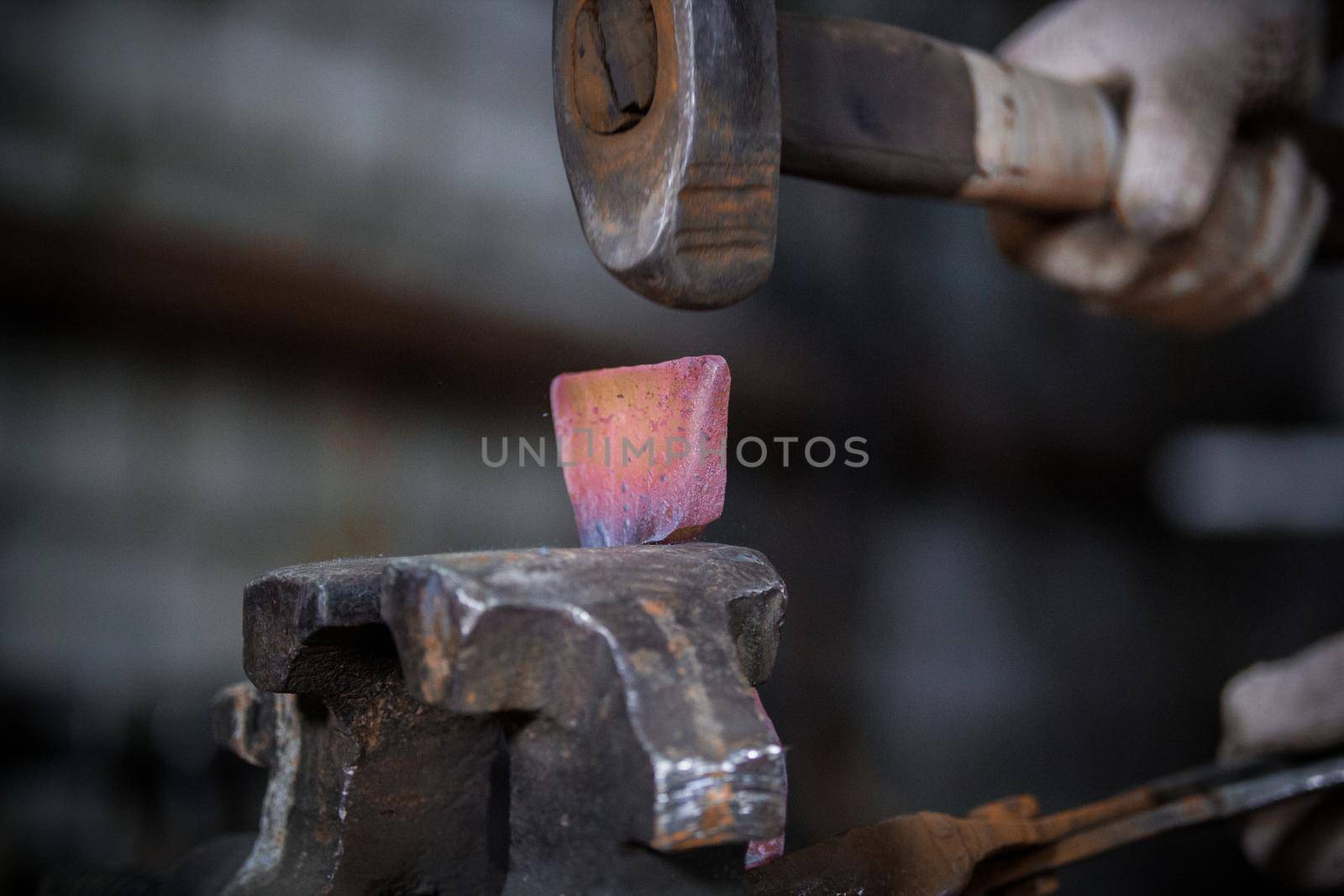 Workspace of blacksmith. Blacksmith working with red hot metal workpiece of new hammer in the vise at the forge. Telephoto shot