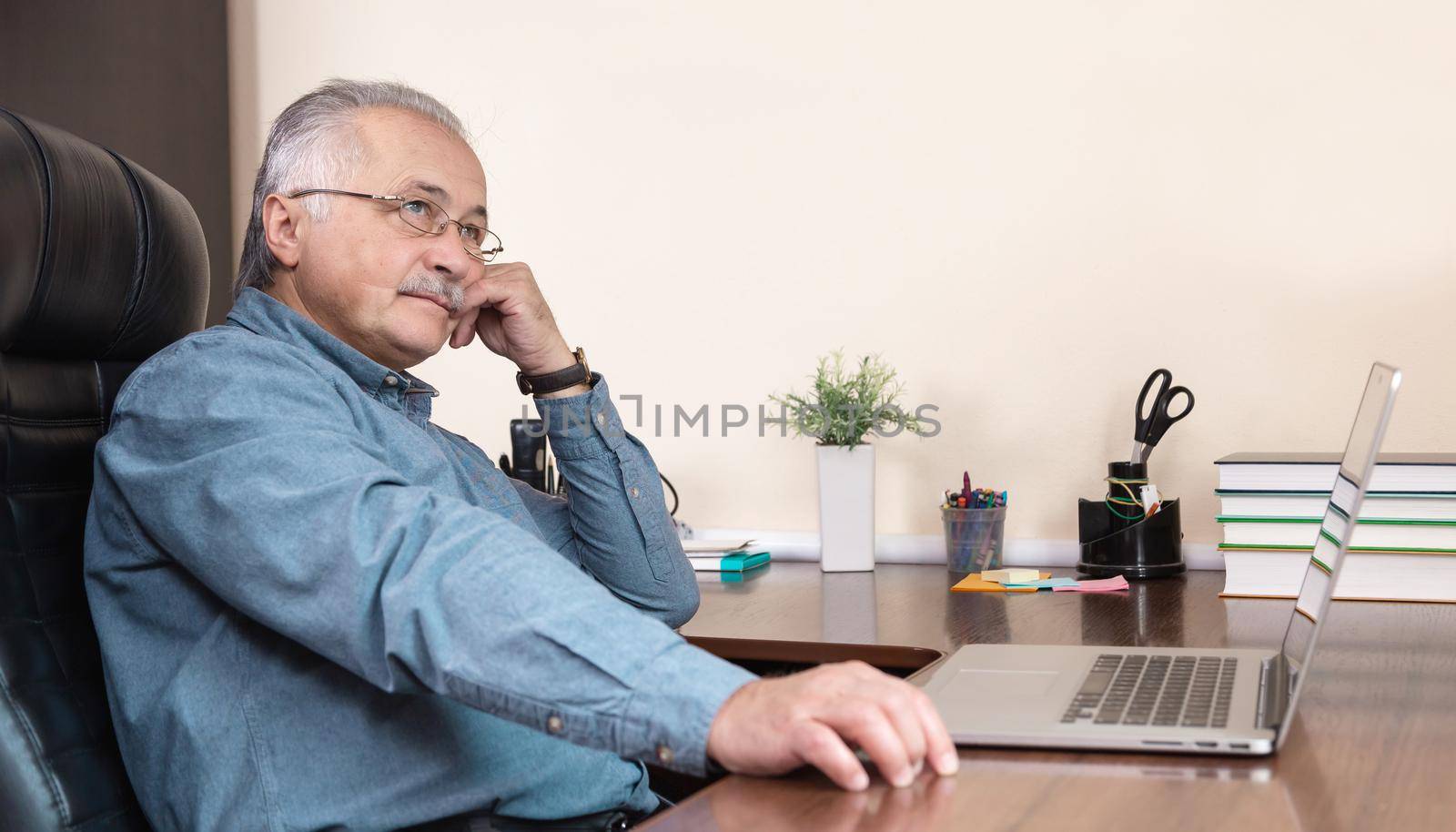 Senior businessman work at home. An elderly man in glasses is working remotely using a laptop. Remote work during coronovirus concept
