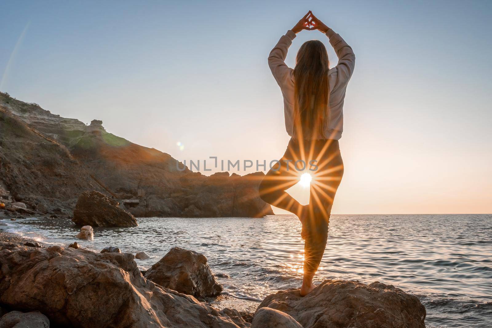 Young woman in swimsuit with long hair practicing stretching outdoors on yoga mat by the sea on a sunny day. Women's yoga fitness pilates routine. Healthy lifestyle, harmony and meditation concept.