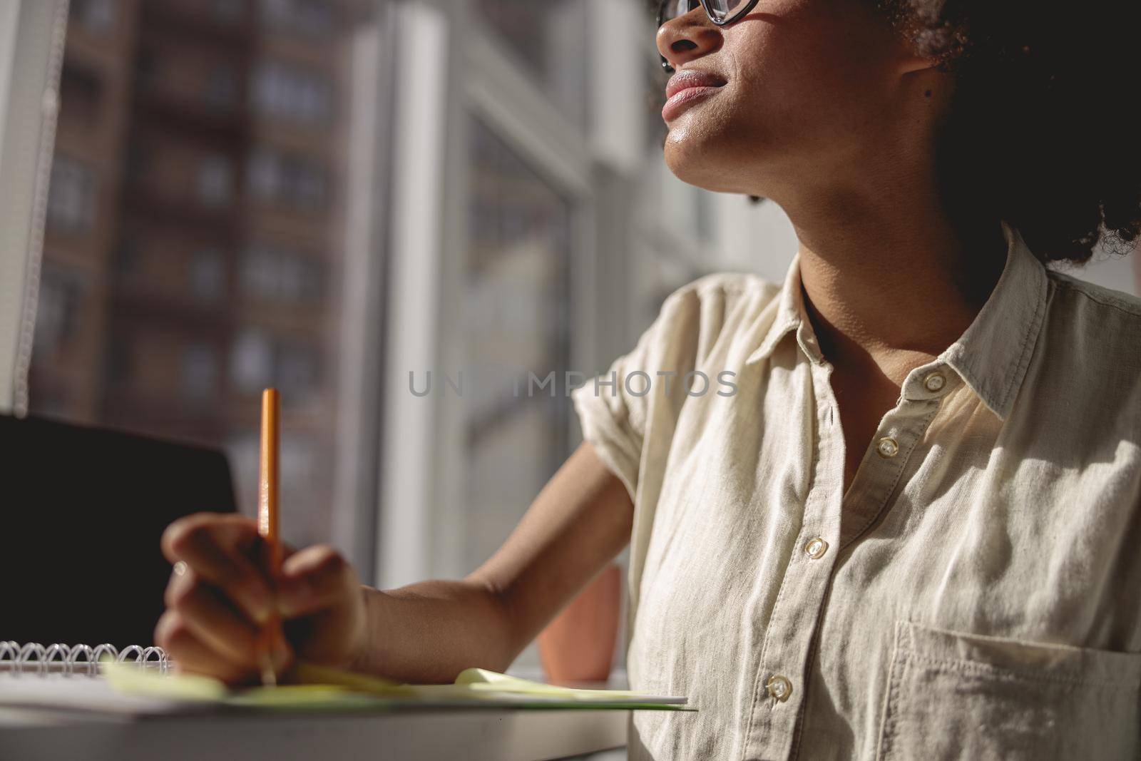 Close up of young multiethnic lady sitting and making notes in notebook during sunny day