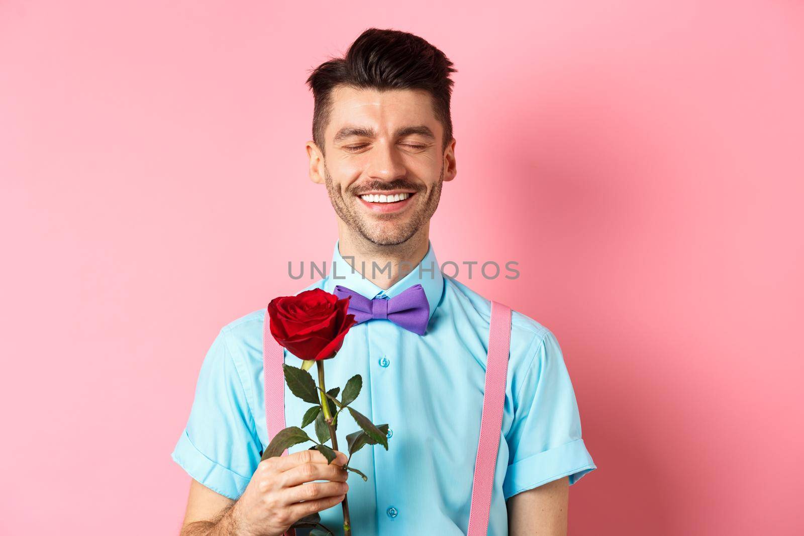 Valentines day and romance concept. Romantic man with red rose going on date with lover, standing in fancy bow-tie on pink background by Benzoix
