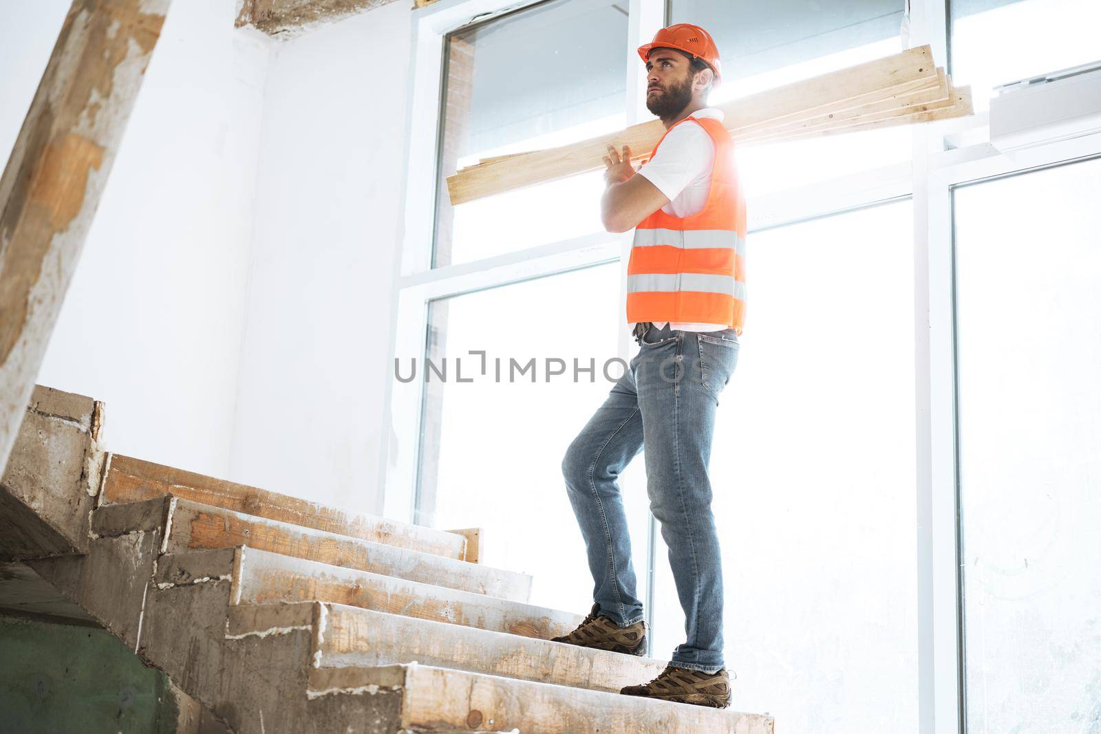 Builder man in hardhat carrying timber on building site, close up portrait