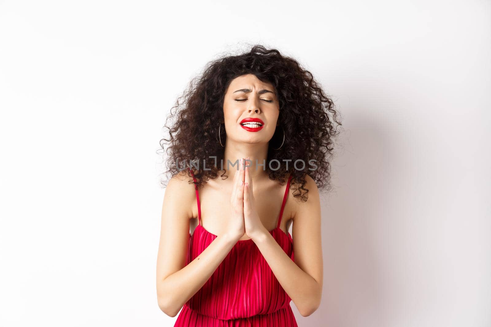 Desperate young woman in red dress begging for help, pleading and looking miserable, supplicating over white background. Copy space