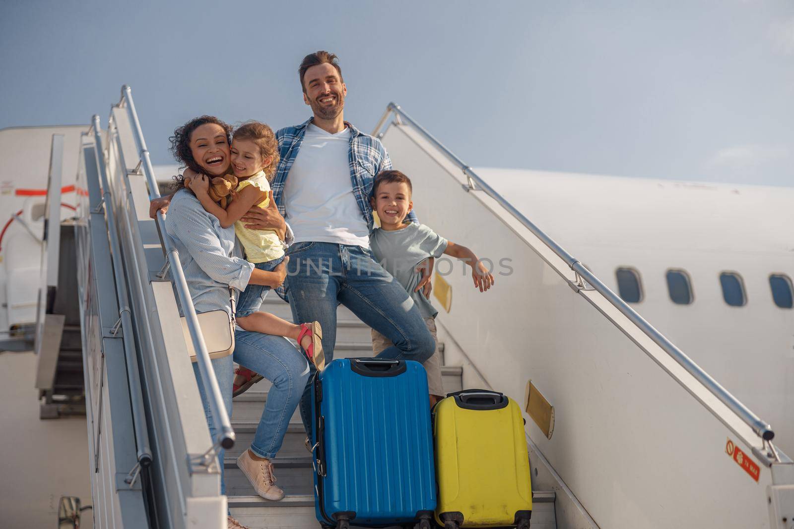 Portrait of happy family of four getting off the plane on a daytime. People, traveling, vacation concept