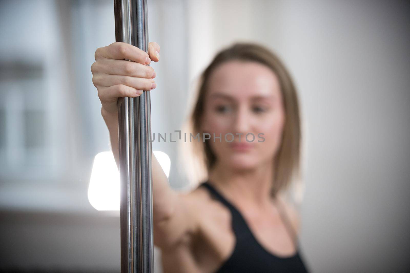 Young attractive woman in sport bra holding a pole. Pole close up