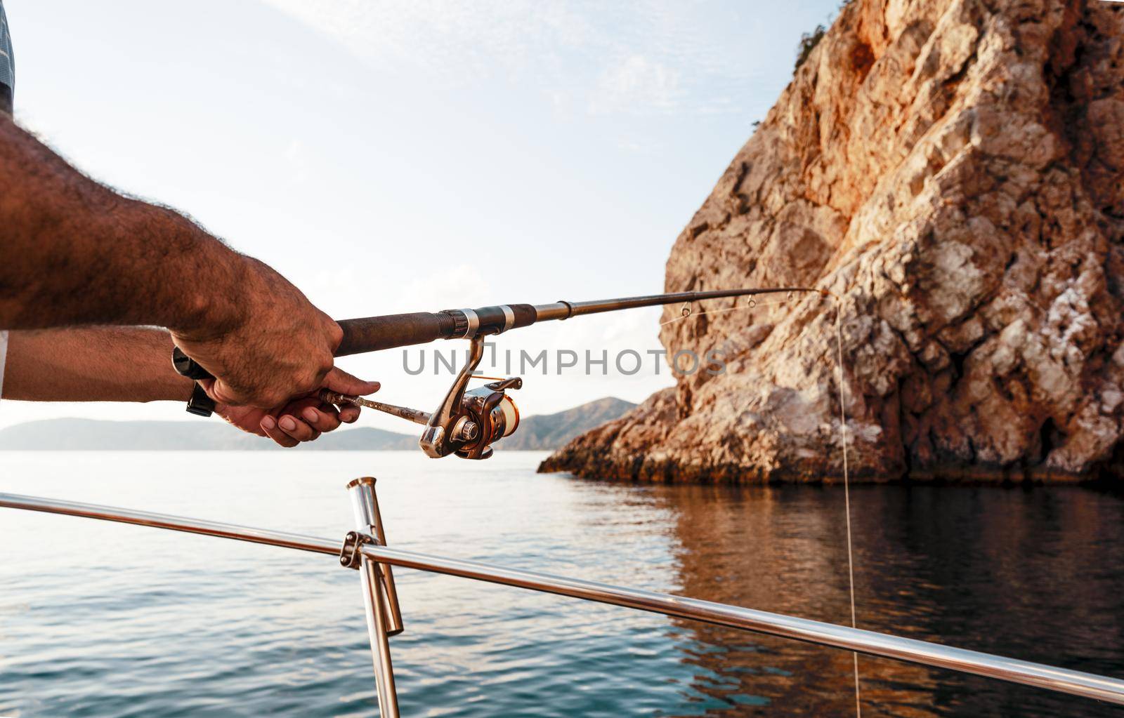 Close up photo of male hands holding fishing rod while fishing on sailboat in open sea