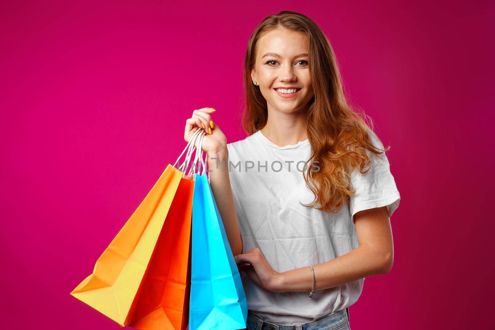 Portrait of happy young smiling woman with shopping bags against pink background