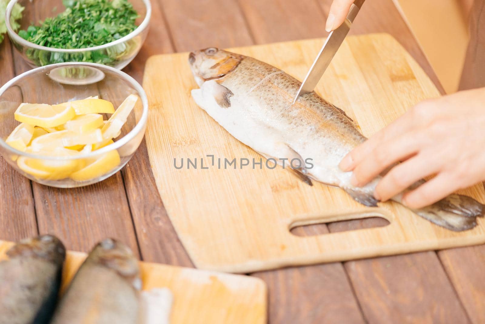 Female hands cutting raw trout fish on kitchen wooden board for seafood dish.