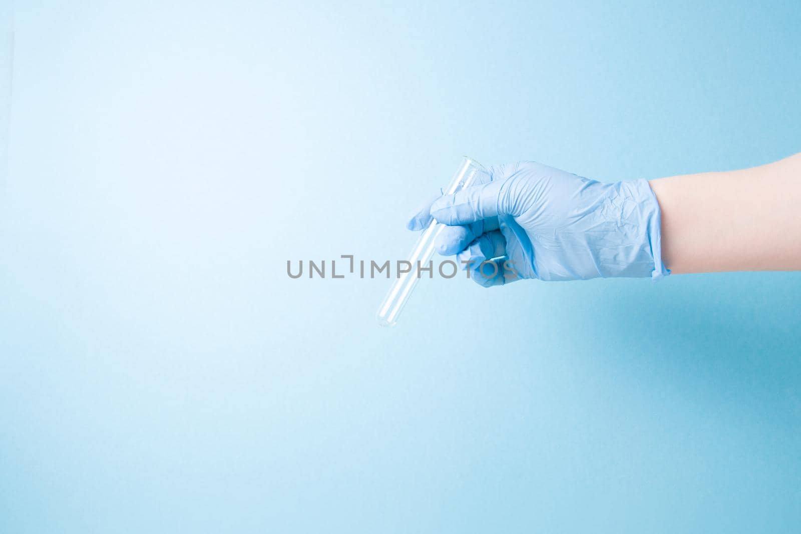 hand in blue disposable medical glove holds a glass empty test tube, blue background copy space