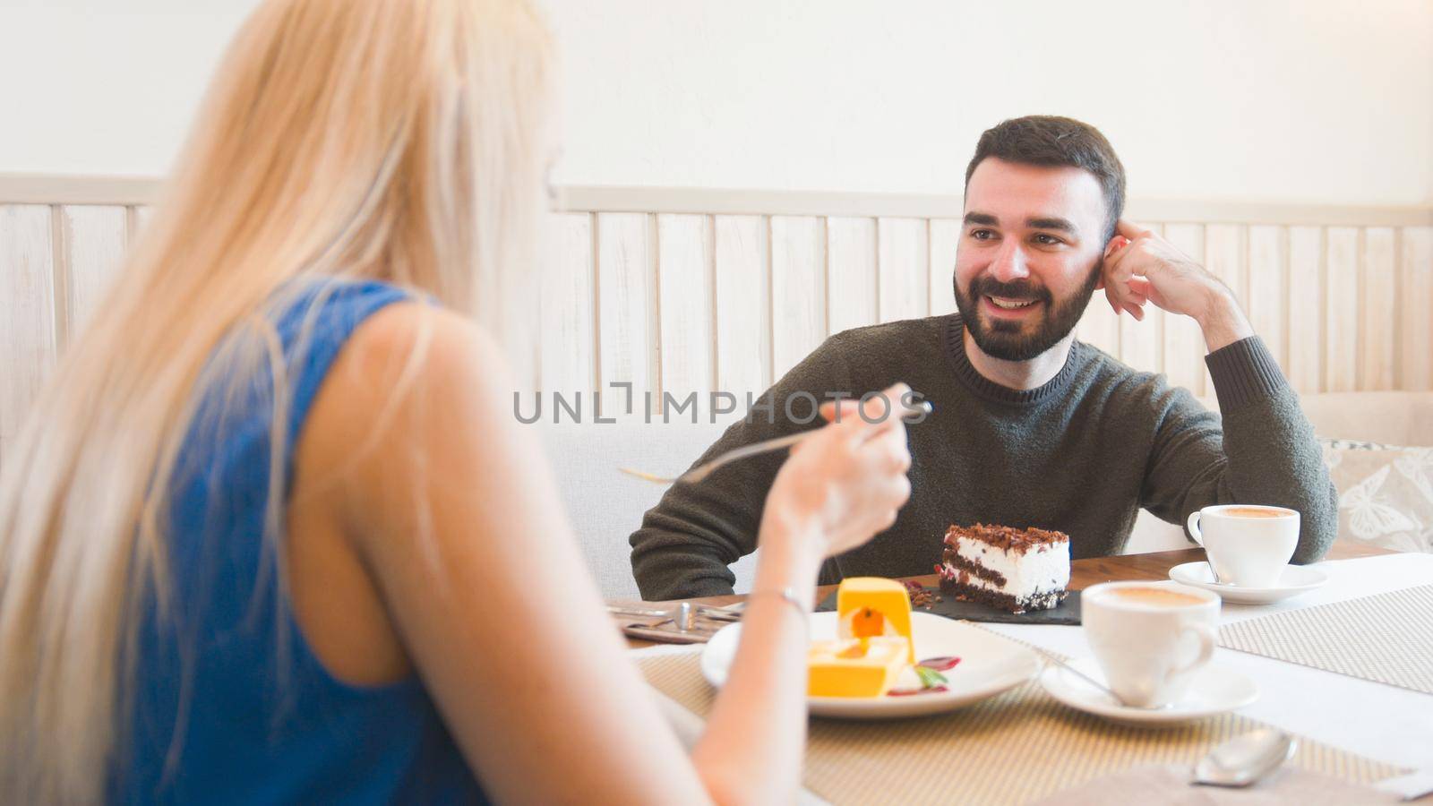 Young caucasian man in front of woman tries desserts in the cafe , close up