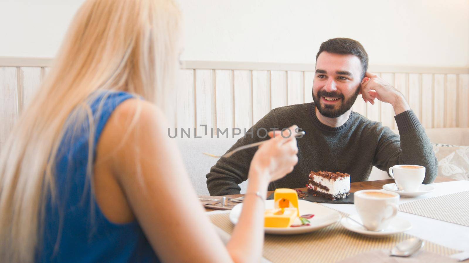 Young caucasian man in front of woman tries desserts in the cafe by Studia72