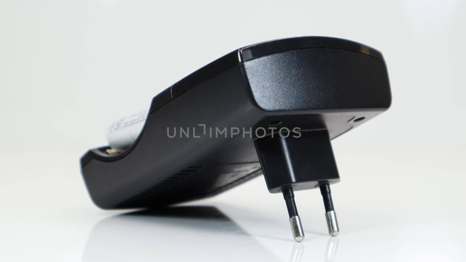 Fast charging of AA batteries. Rechargeable batteries in a black charger with four battery cells on a white background