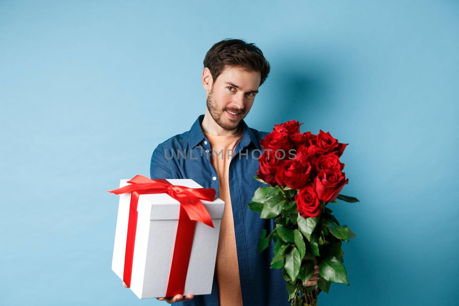 Love and Valentines day concept. Romantic man giving you gift box and bouquet of flowers on date, standing over blue background.