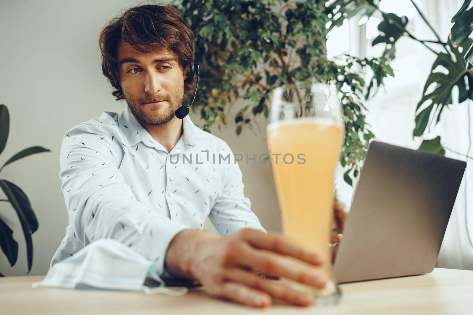 Bearded man using his laptop while drinking glass of beer sitting at his table