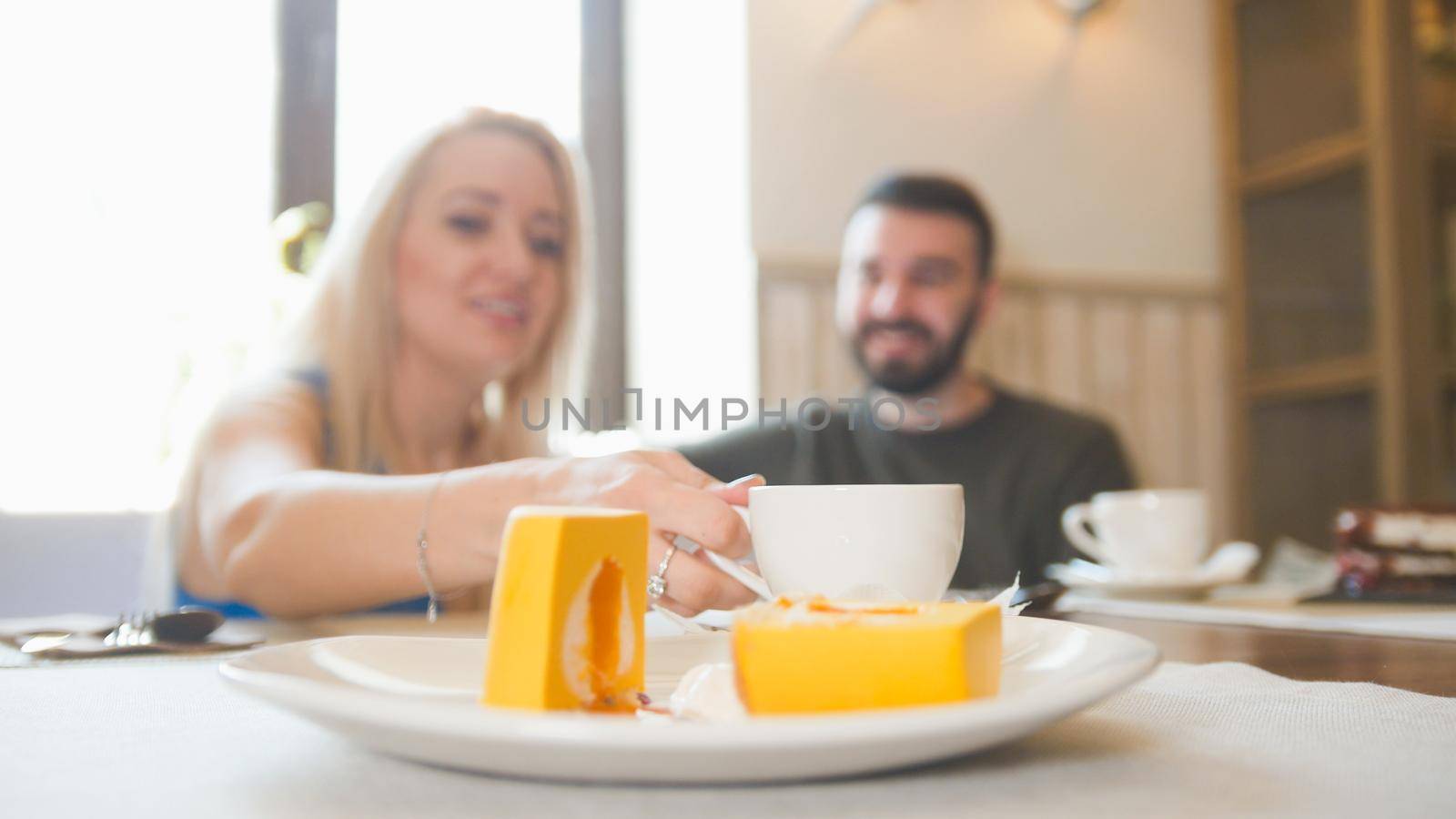 Sweet dessert in front of couple sitting in a cafe drinks coffee and laughing, close up