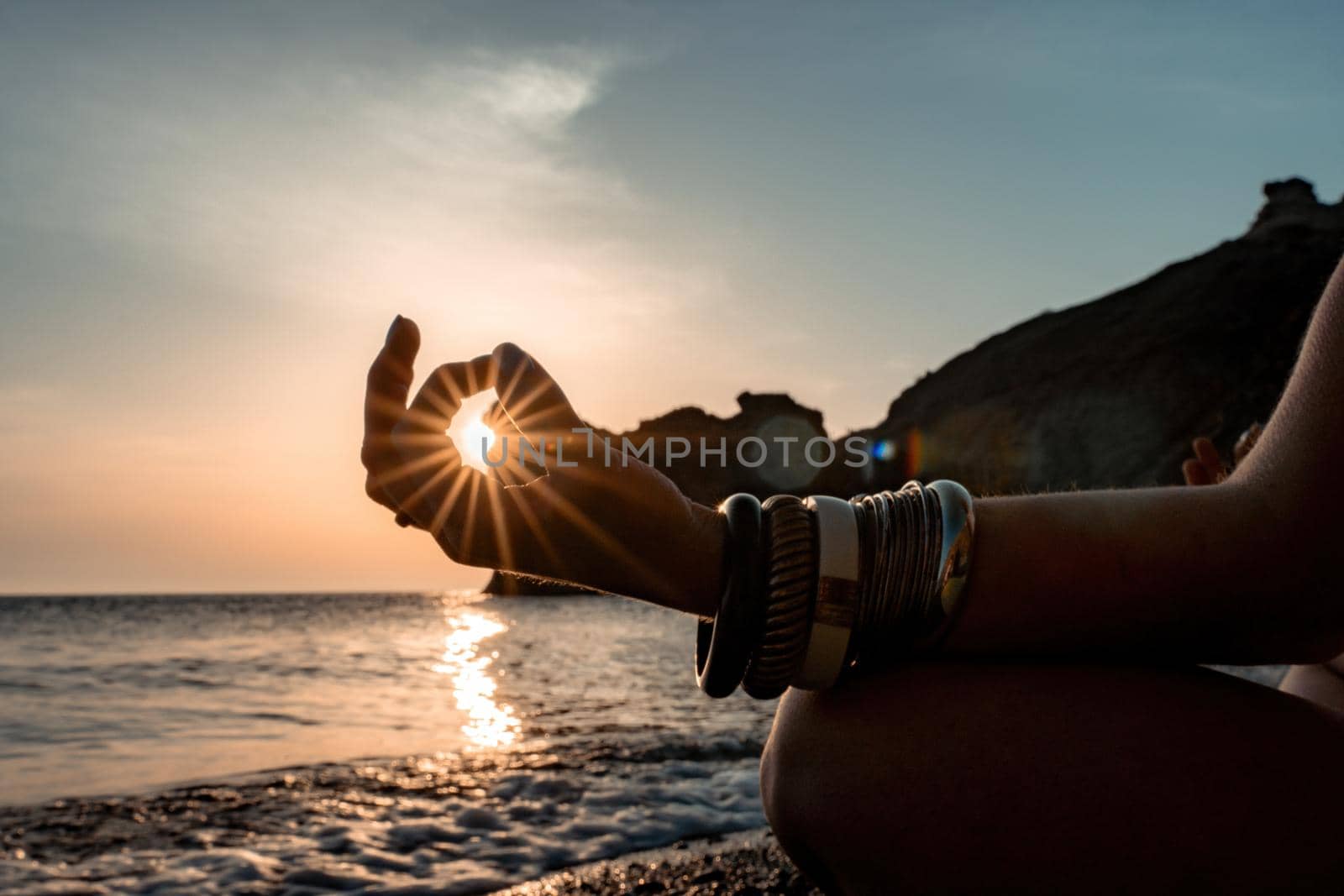 Young woman with long hair in white swimsuit and boho style braclets practicing outdoors on yoga mat by the sea on a sunset. Women's yoga fitness routine. Healthy lifestyle, harmony and meditation by panophotograph