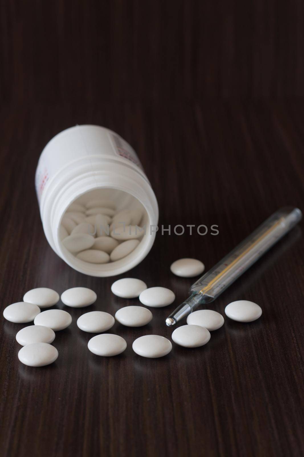 Pills from a jar and body temperature thermometer on a dark background