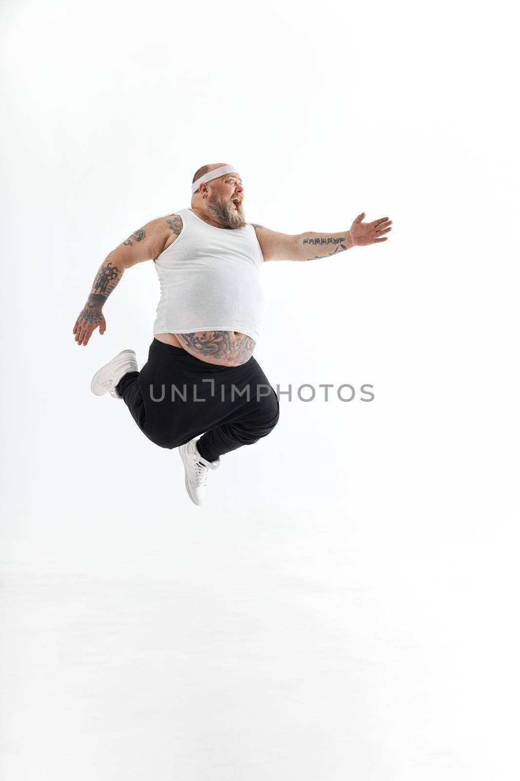 Happy fat man with big belly and tattoes in sports wear posing on white background by Yaroslav_astakhov