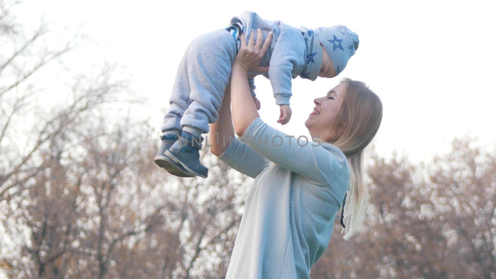 Young mother and her little baby playing in autumn park. Mother holding a baby. Bright sky.Wide shot