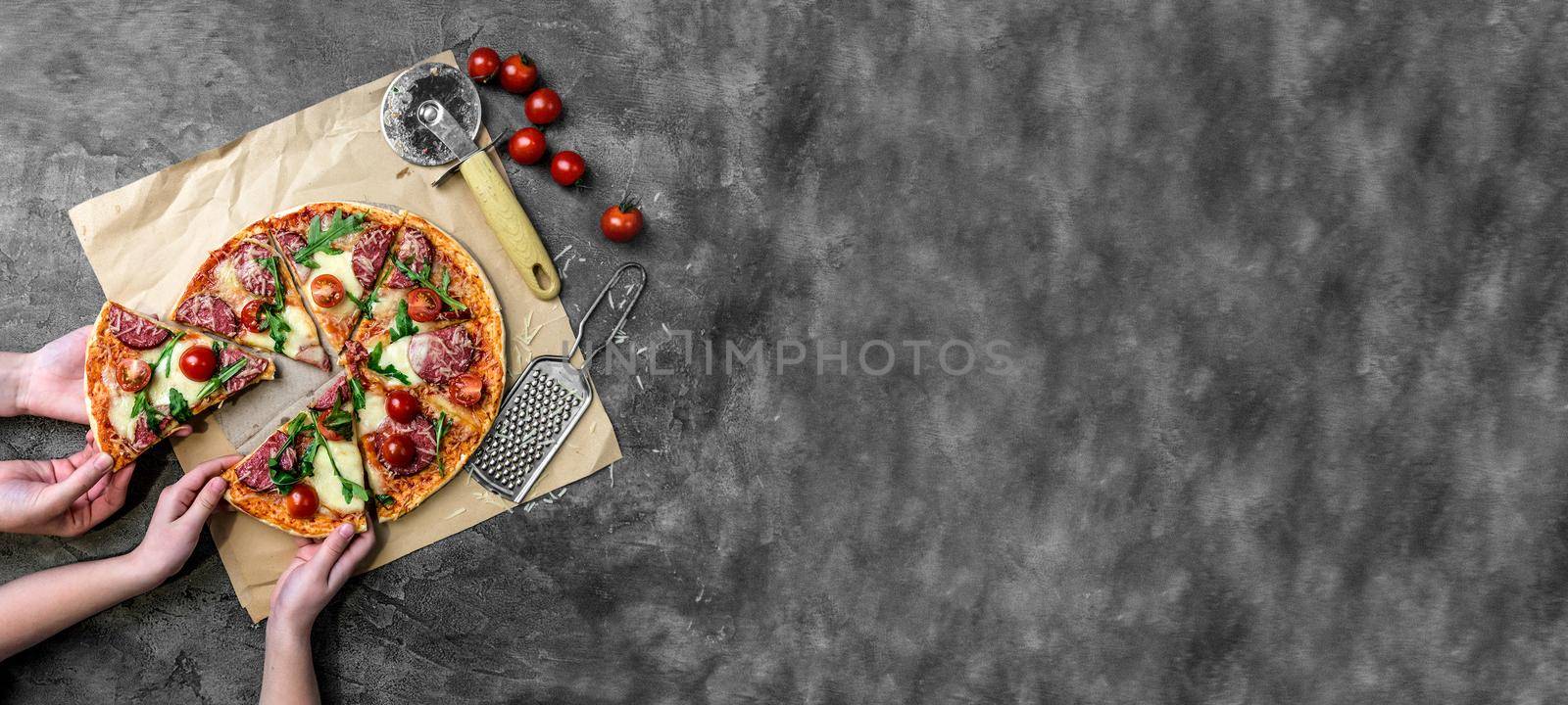 children's hands take homemade pizza with salami, cherry tomatoes and rucola