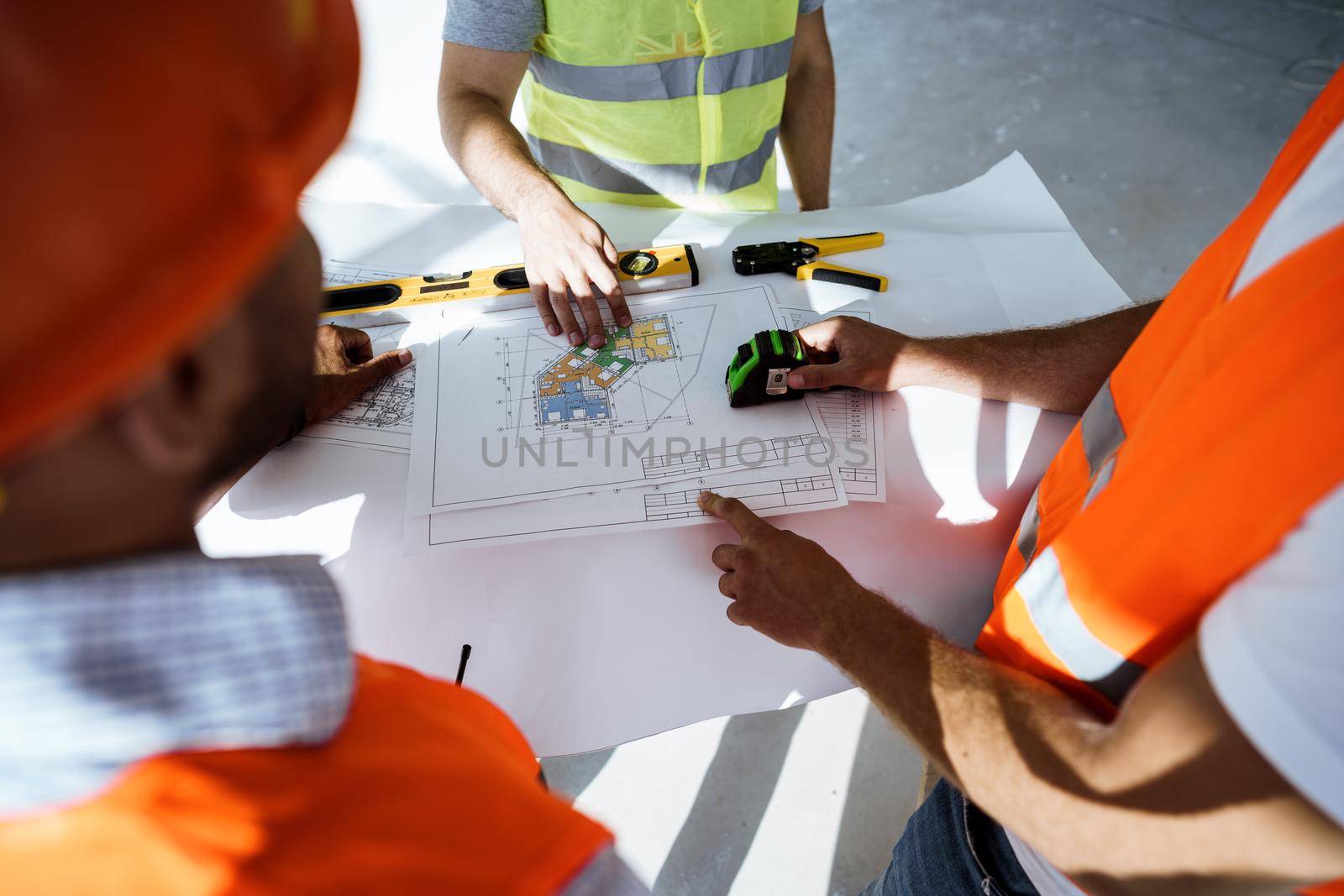 Close up photo of three man engineers looking at blueprint on construction site