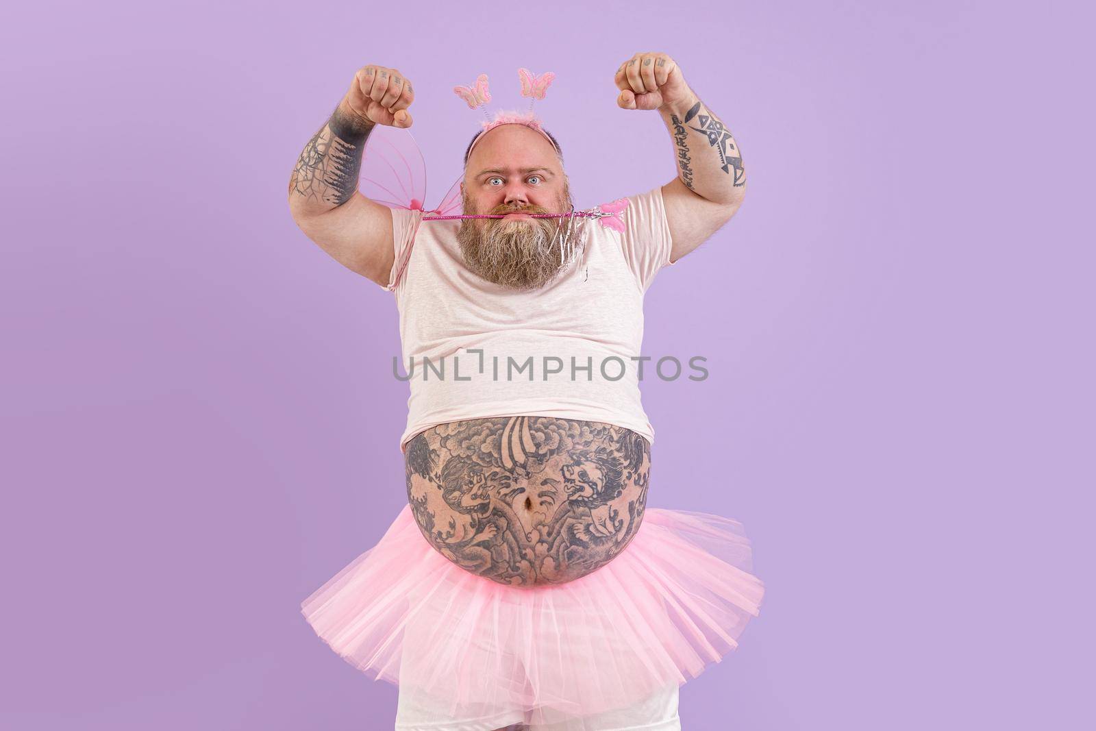 Mature plus size man with tattoos in fairy costume shows muscles on purple background by Yaroslav_astakhov