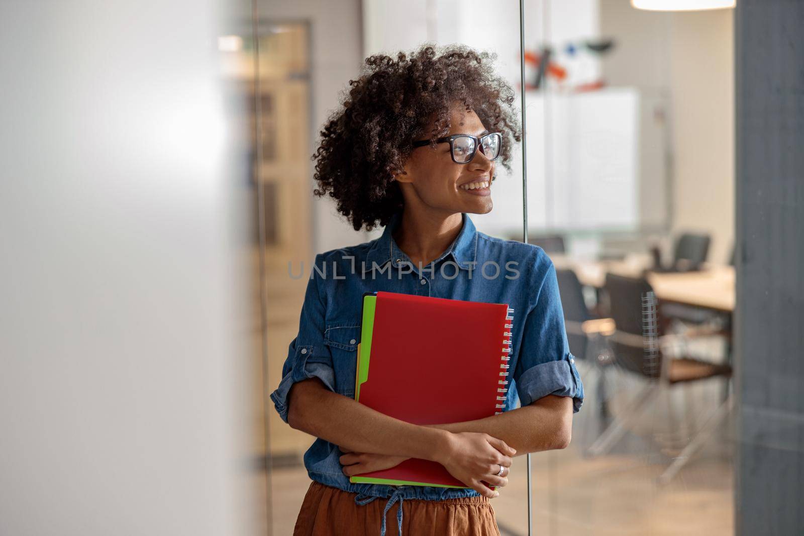 Smiling pretty woman standing in the office while holding documents and looking away