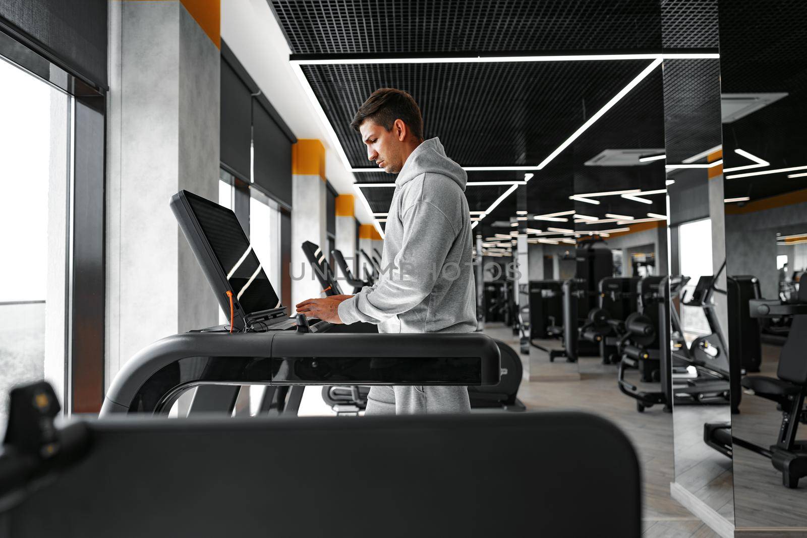 Portrait of a young man in orange windbreaker workout on a fitness machine at a gym.