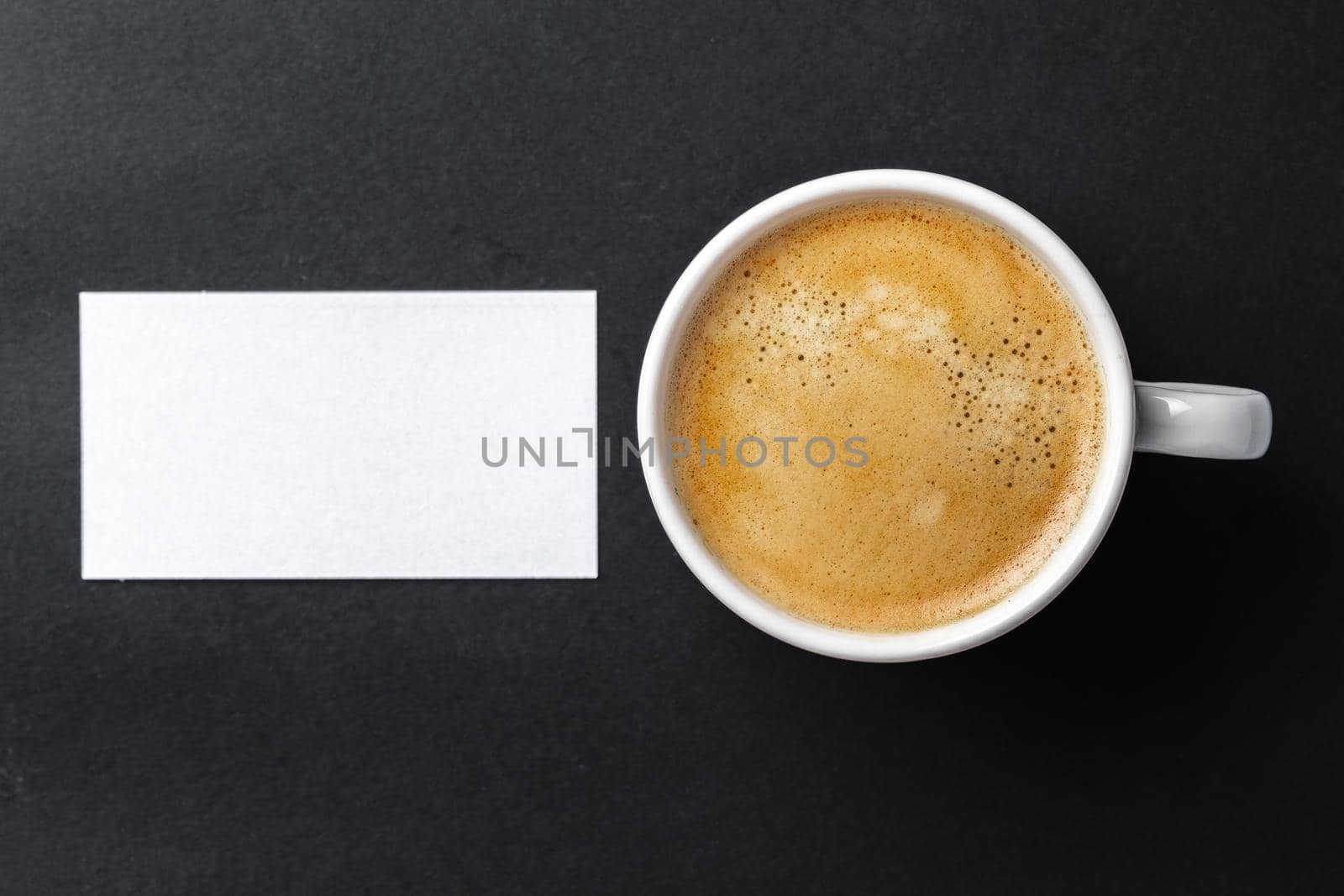 Top view of cup with espresso and white business card template on black table