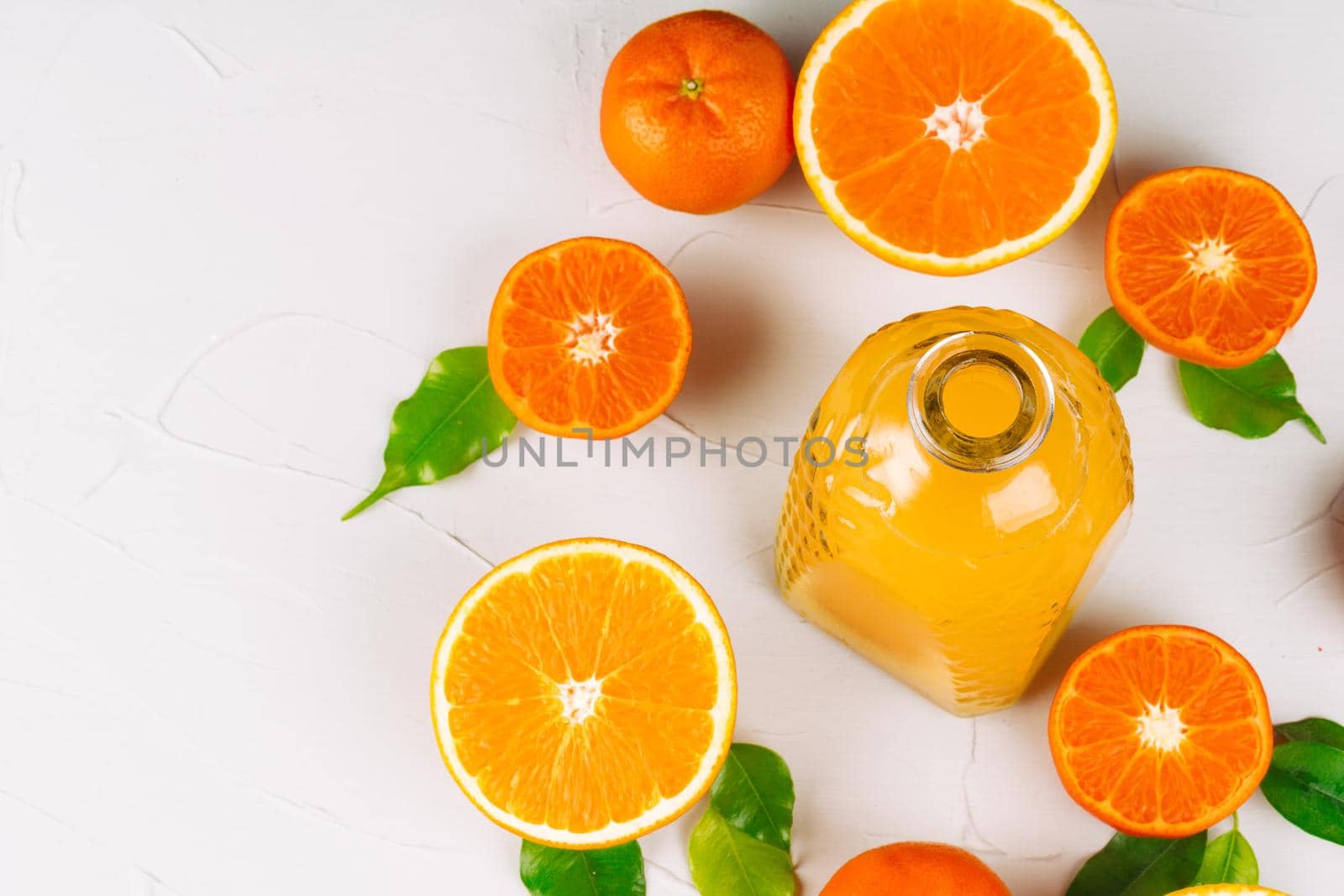 Glass bottle of orange juice with halves of ripe oranges. Close up.