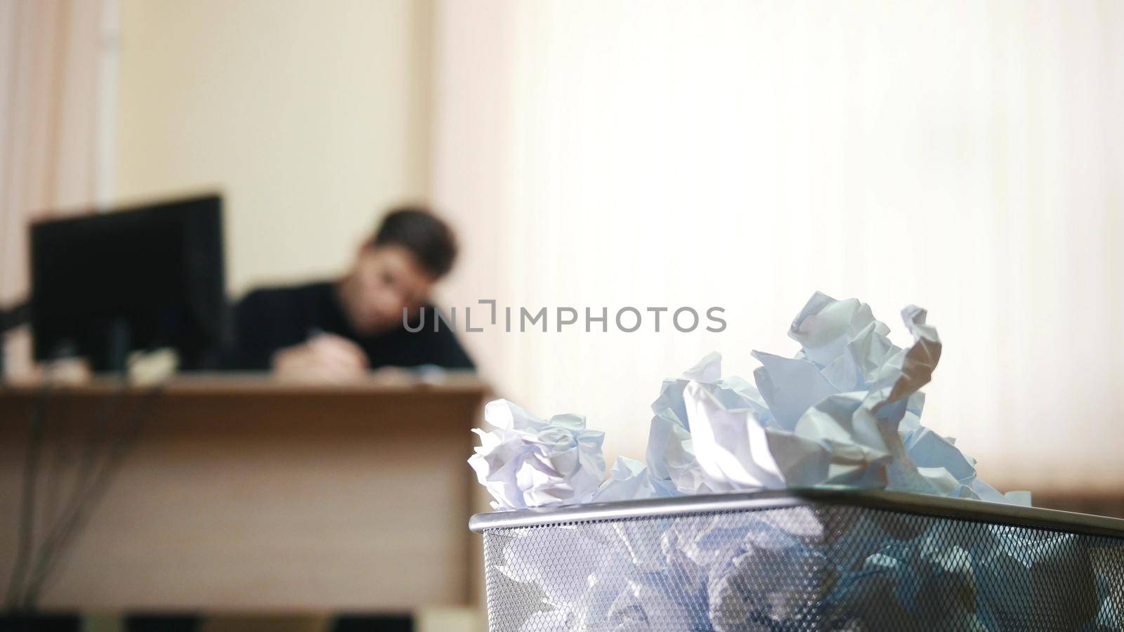 A man in office writing something, focus on the trashcan. Close up