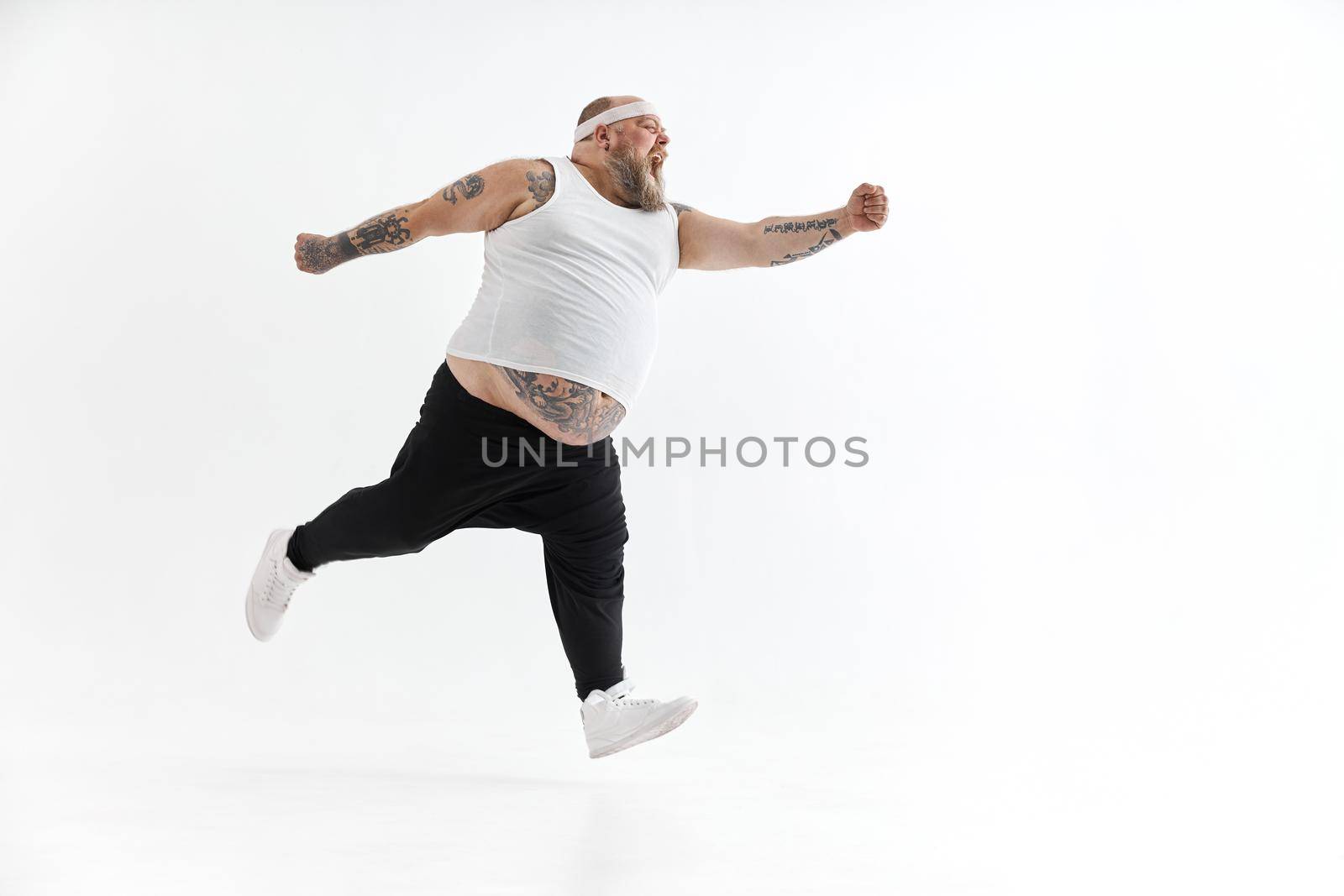 Happy fat man with big belly and tattoes in sports wear posing on white background