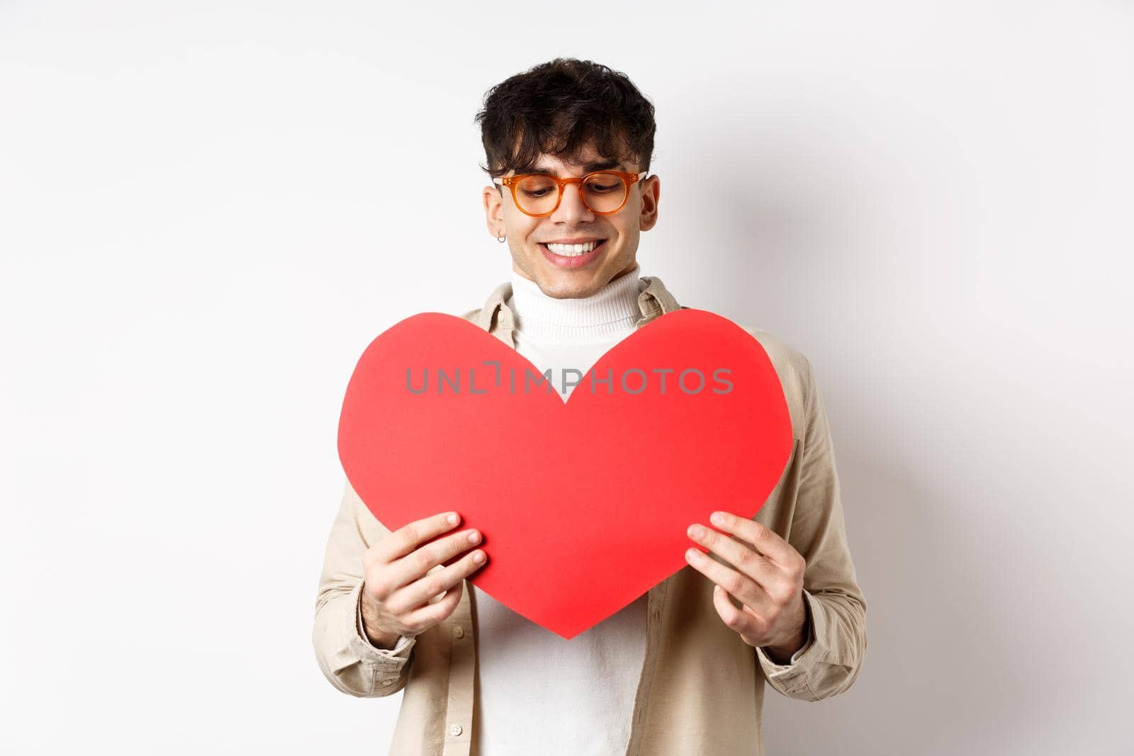 Handsome and stylish man in sunglasses, prepare surprise postcard for girlfriend on Valentines day, holding big red heart cutout and smiling happy, standing over white background by Benzoix