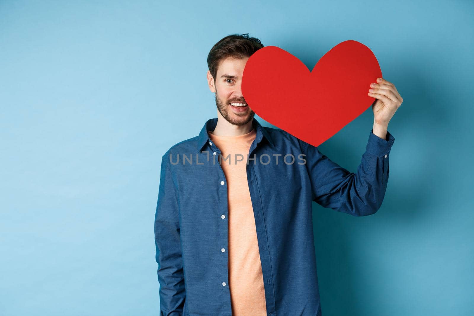 Happy man showing valentines heart and smiling, make romantic gift on lovers day, standing over blue background by Benzoix