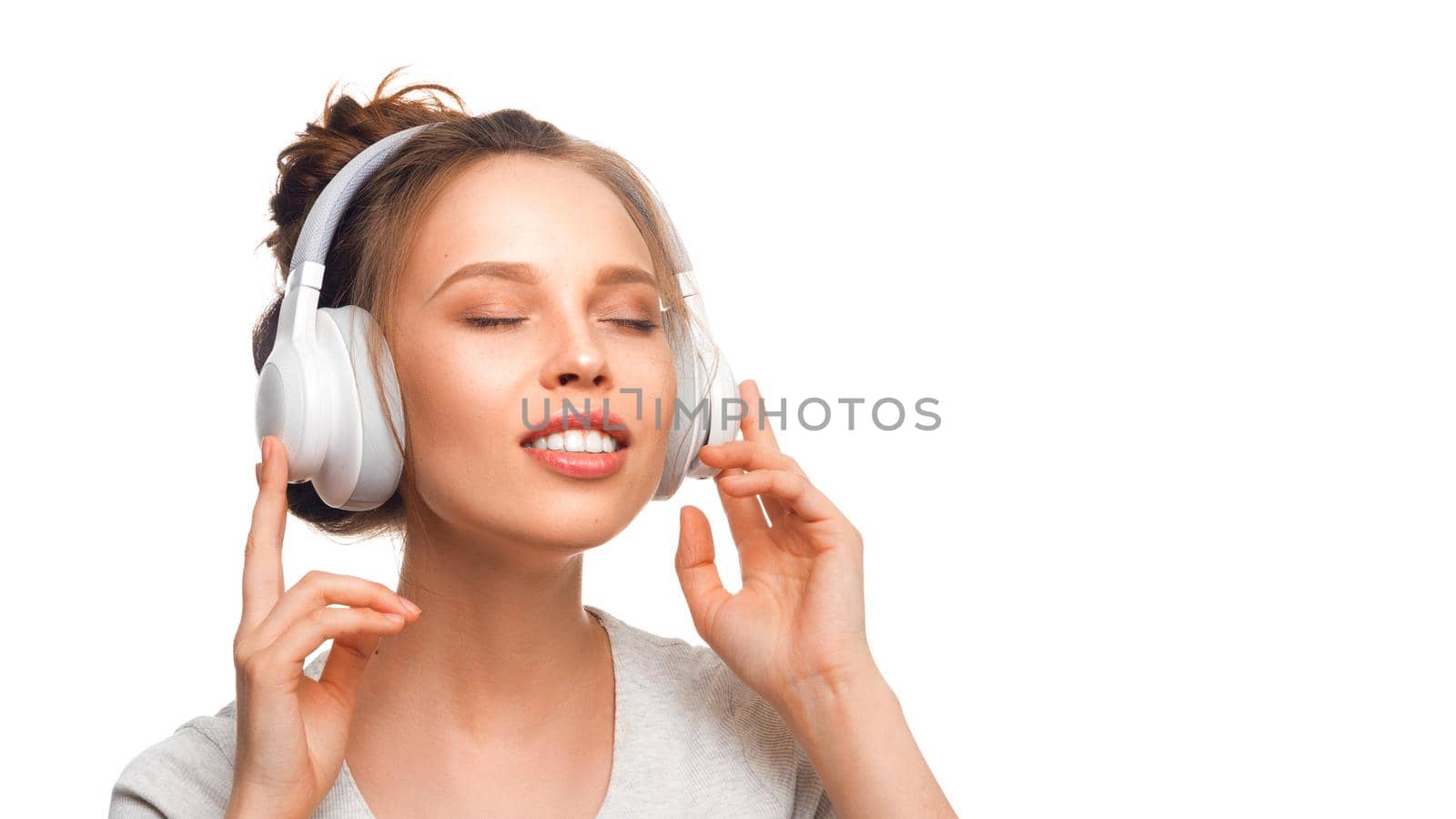 Attractive girl with closed eyes listening to the music via headphones on white background. Sound groove with closed eyes. Close up