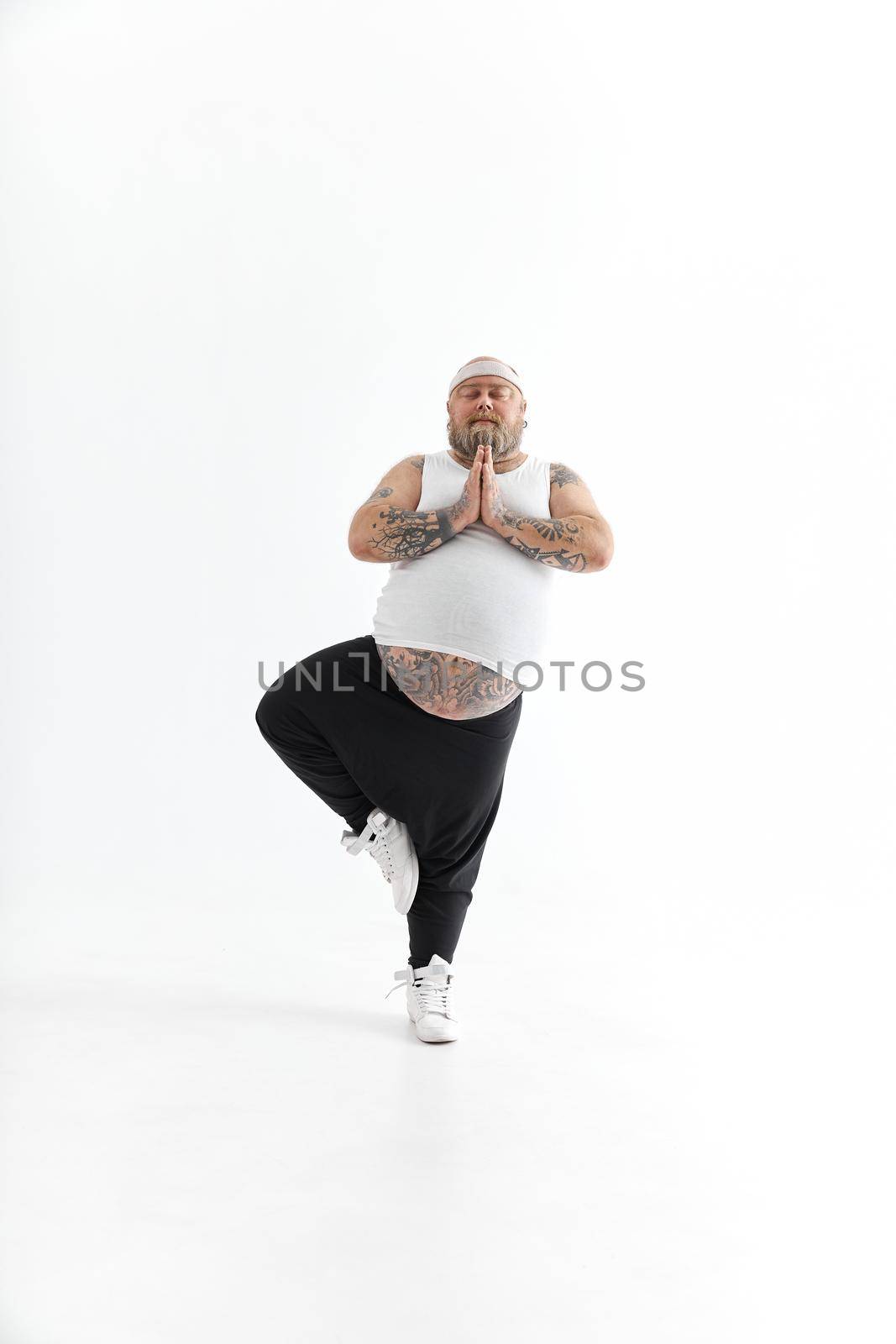 Happy fat man with big belly and tattoes in sports wear posing on white background