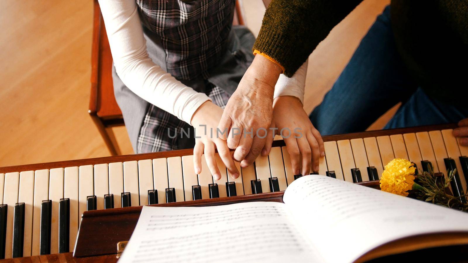 A little girl playing piano on music lesson. A teacher helping her. Hands close up